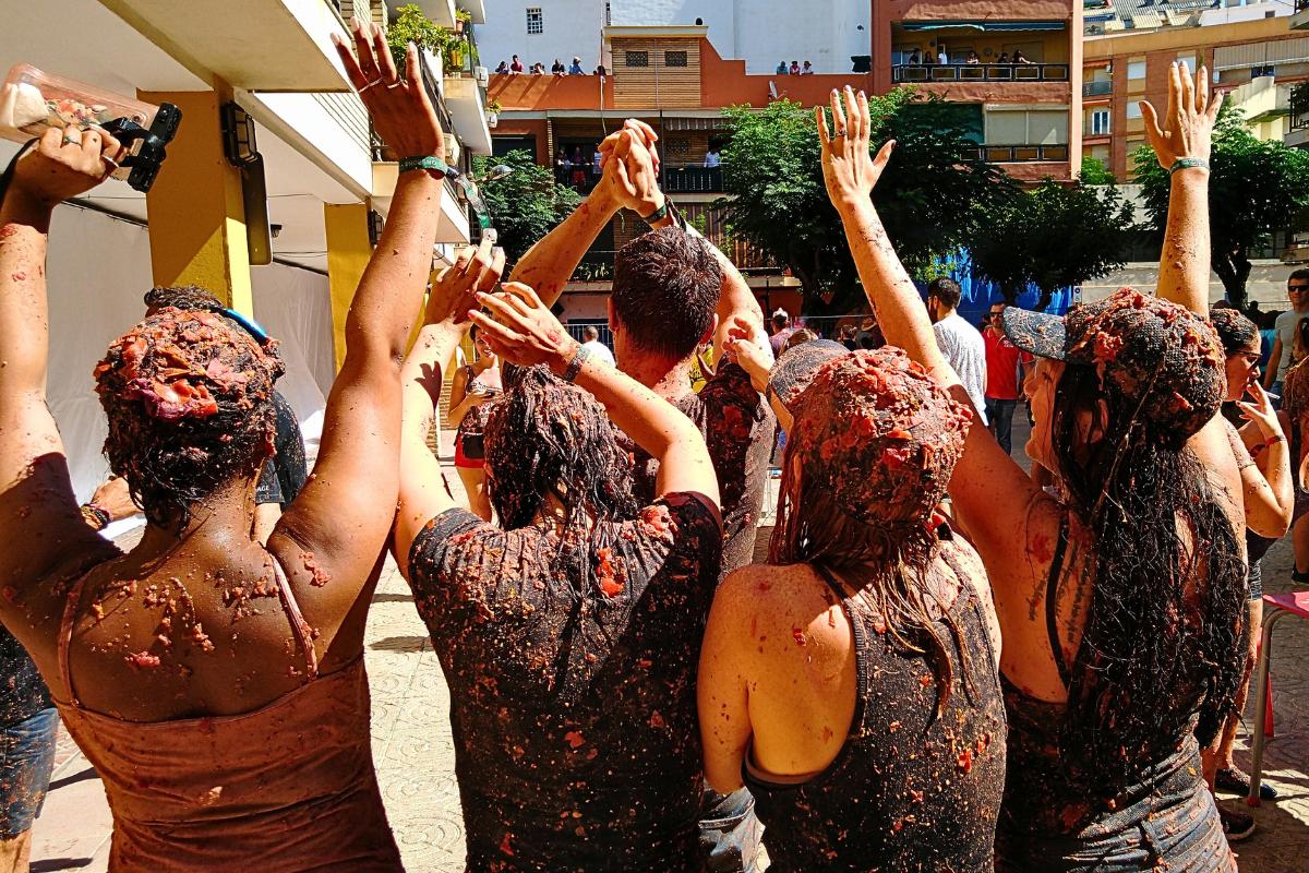 Facts About La Tomatina featuring a group photograpahed from behind covered in tomatoes
